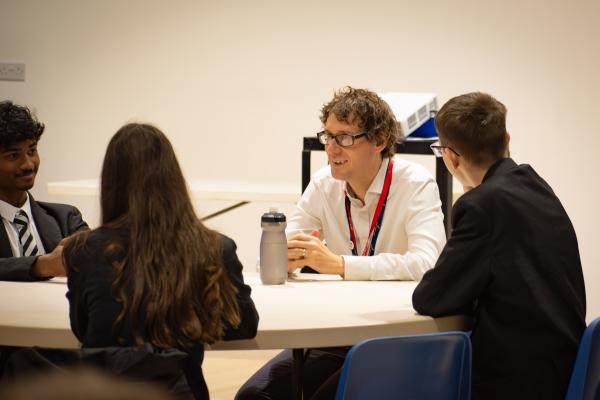 Photo of a visitor and students sat around a table in discussion